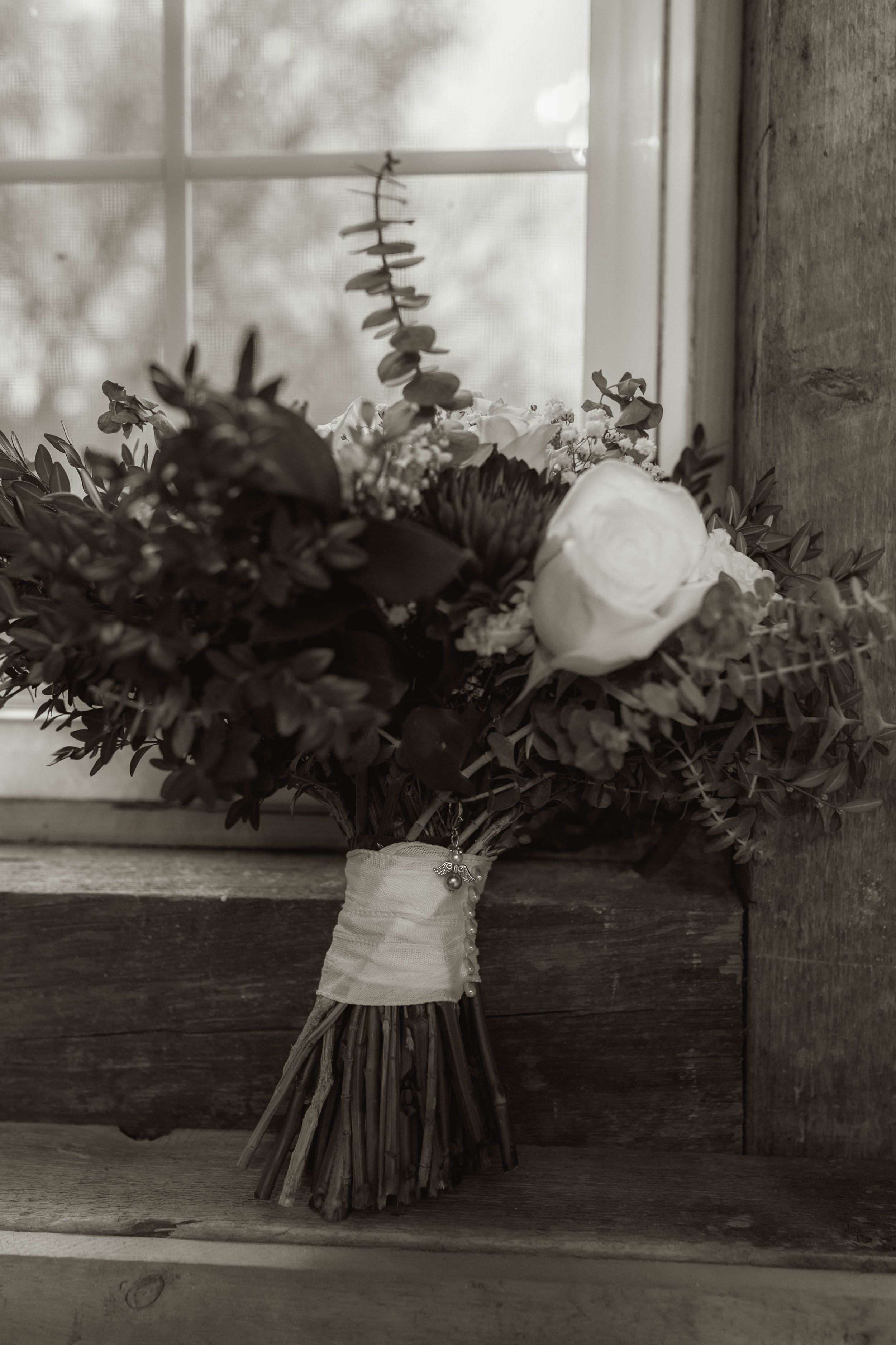 Black and white photo of wedding bouquets arranged on a wooden windowsill.