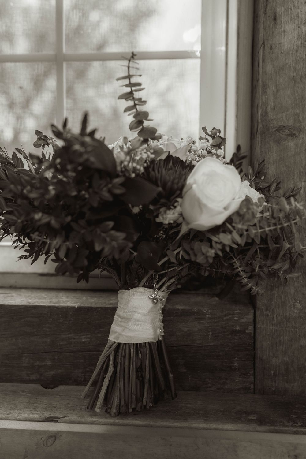 Black and white photo of wedding bouquets arranged on a wooden windowsill.