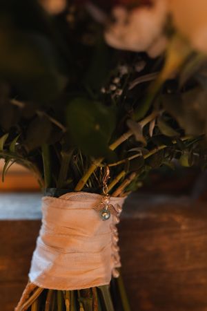 Close-up detail of a bridal bouquet wrapped in white ribbon with delicate charm accents.