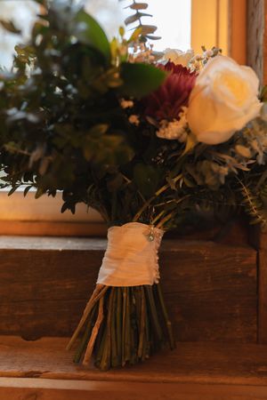 Wedding bouquet with white roses and burgundy flowers wrapped in elegant white fabric.