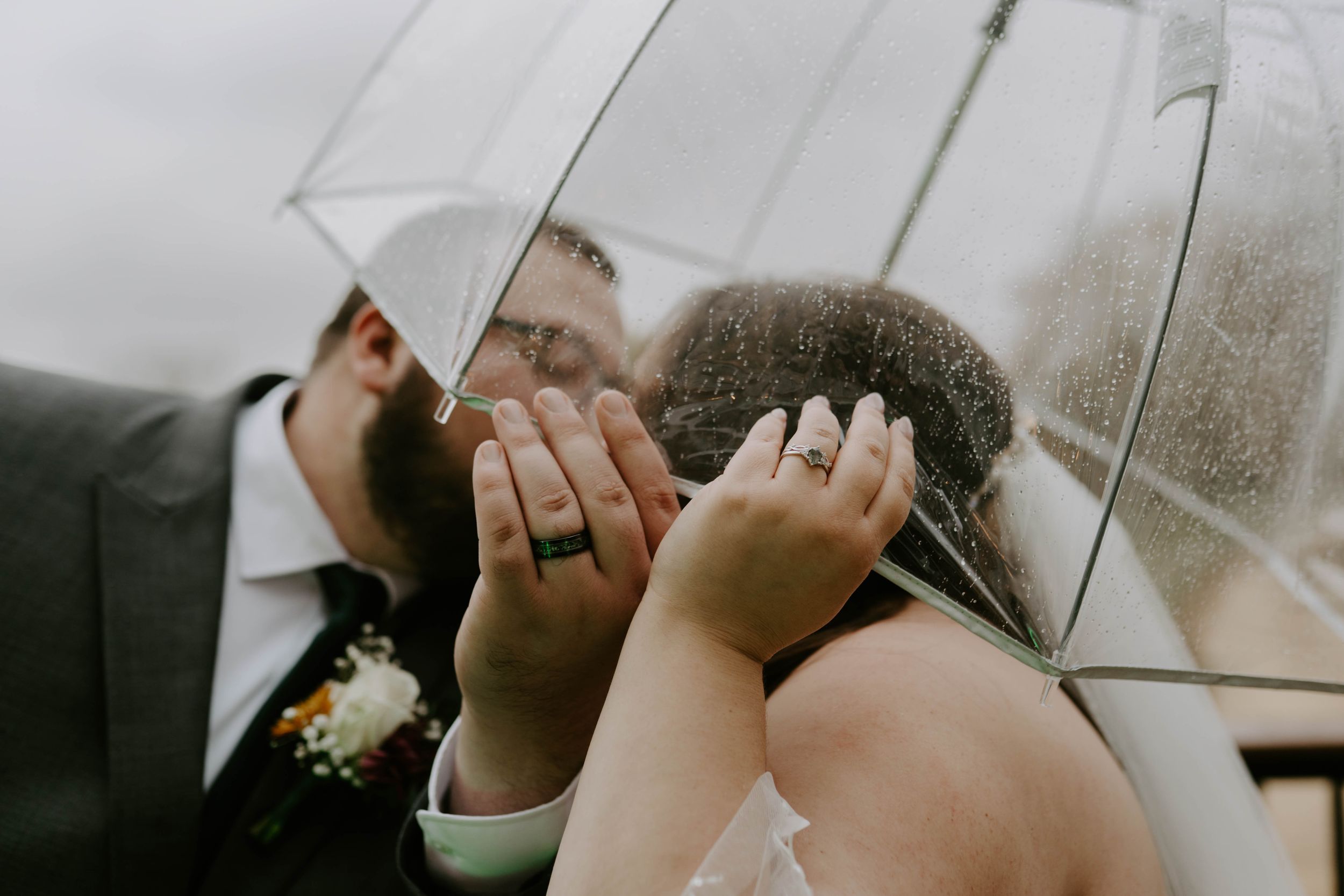 Romantic wedding photos under clear umbrellas on an overcast day.