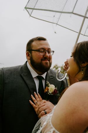 A romantic wedding photo of a couple sharing a joyful moment under an umbrella on an overcast day.