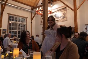 Wedding reception guests gathered around tables with glowing candles in a rustic venue.