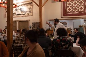 Wedding reception guests dining in a rustic venue with wooden beams and quilt decor.