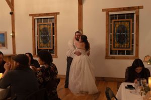 Guests dancing together at a wedding reception in a rustic venue with wooden beams and warm lighting.