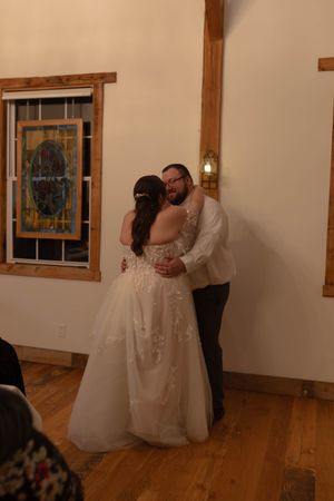 Couple sharing their first dance in a rustic venue with wooden beams and windows.