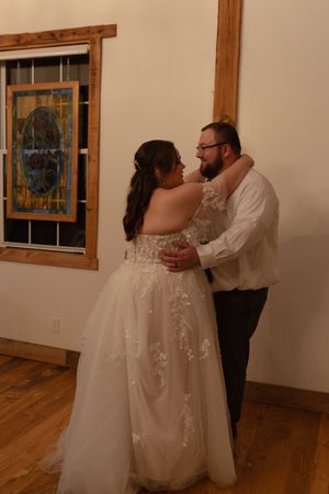 Couple dancing in an elegant ballroom with hardwood floors and stained glass windows.