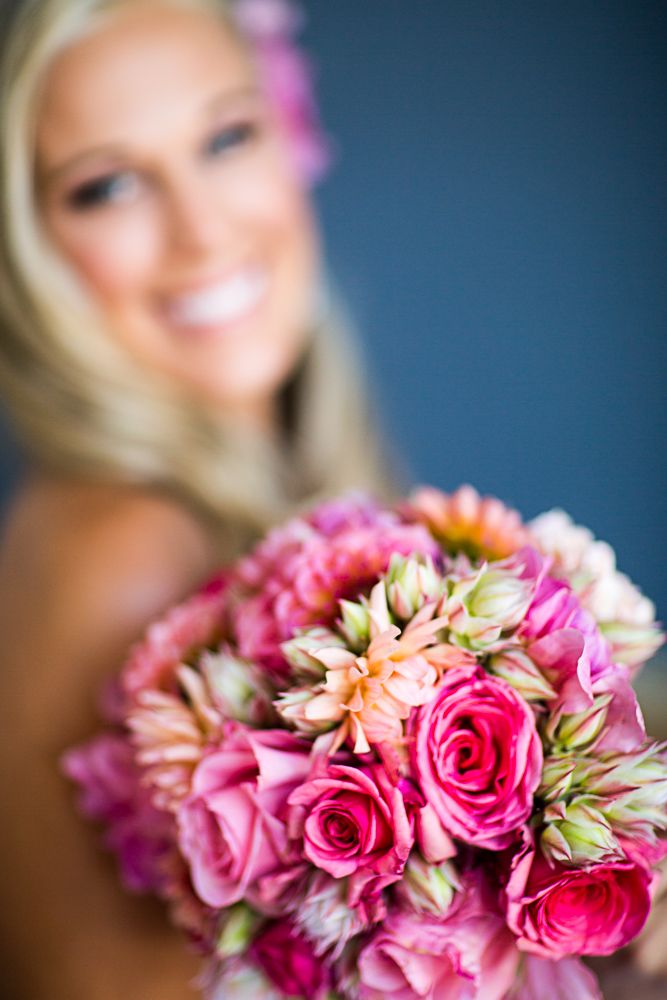 A vibrant pink and peach rose bouquet in soft focus with blurred background creates an elegant wedding detail shot.