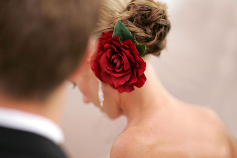 A vibrant red rose adorns an elegant updo hairstyle against a soft brown background.