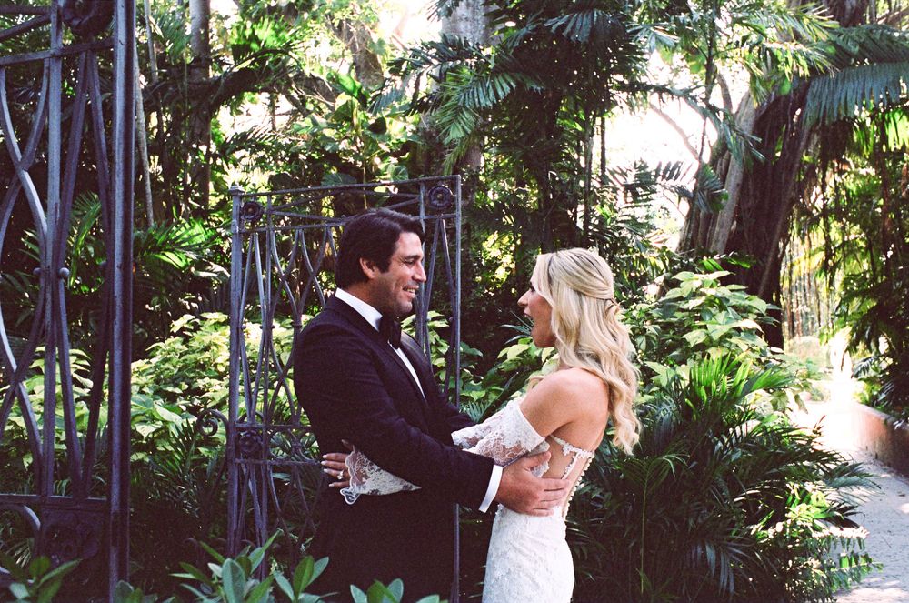 A couple shares a romantic dance moment surrounded by lush tropical garden foliage and palm trees.