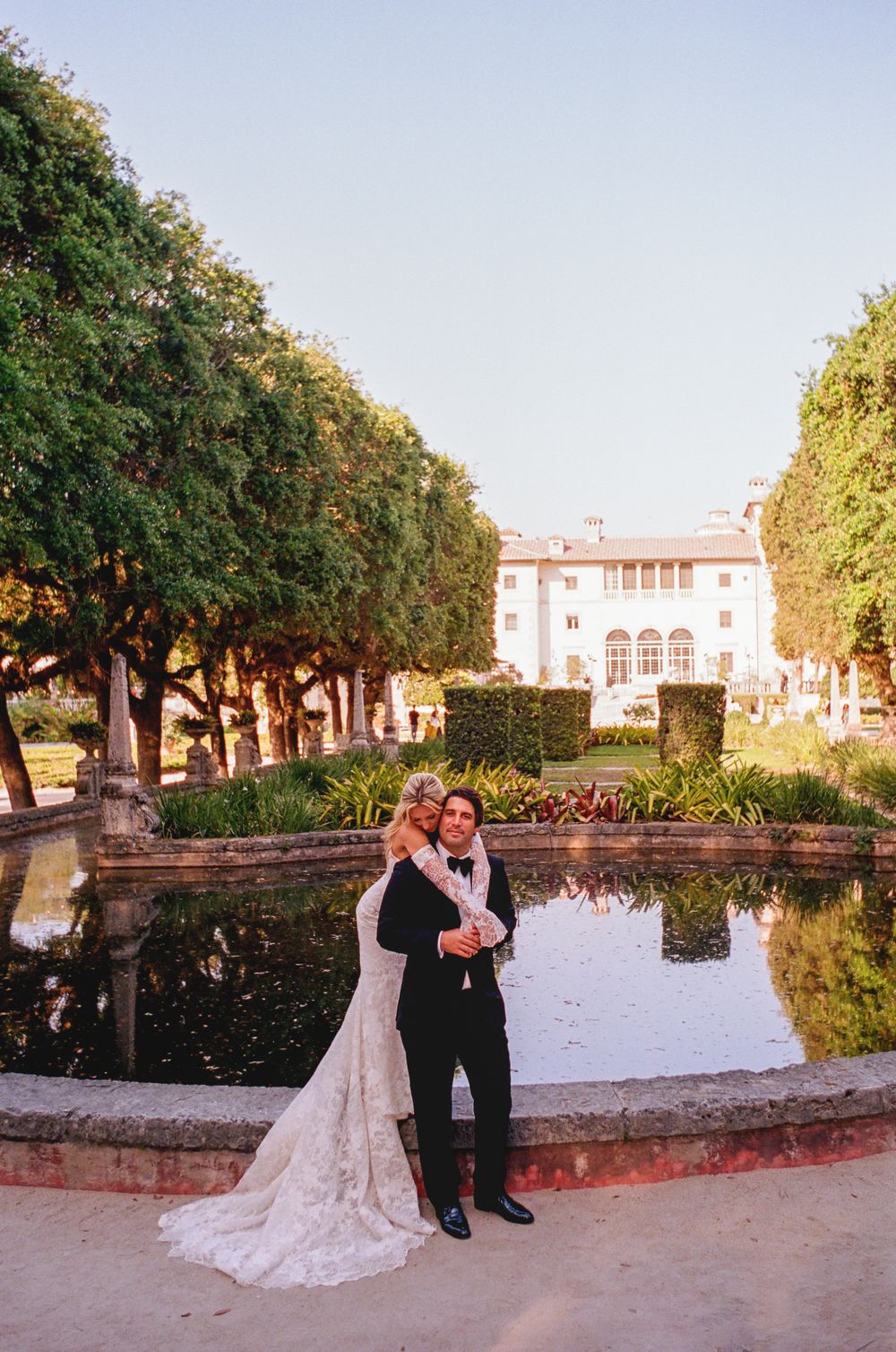 Couple poses for romantic sunset photos at an elegant garden estate with reflecting pool and historic architecture.