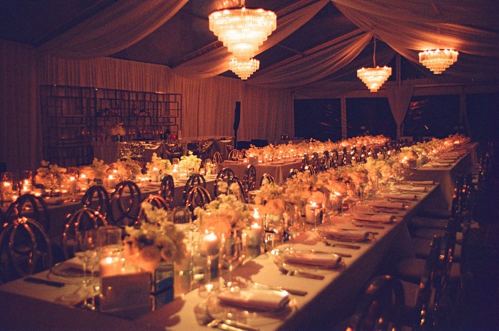 Elegant wedding reception tables decorated with glowing chandeliers and warm ambient lighting create a romantic atmosphere.