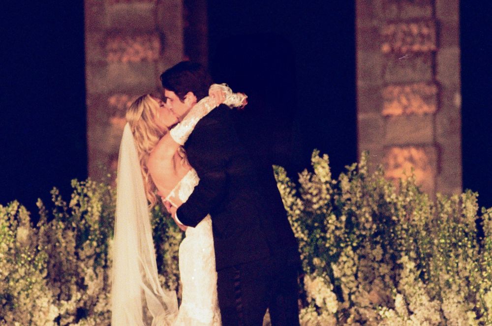 Bride and groom sharing a romantic first dance kiss outdoors at night, surrounded by white flowers.