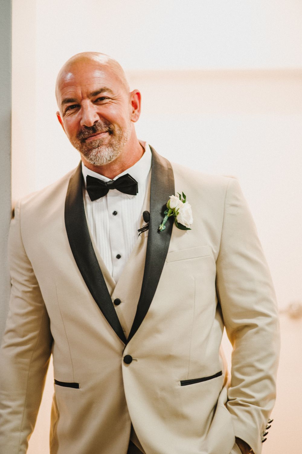 A groom wearing a cream-colored tuxedo with black lapels and bowtie smiles in a sequence of wedding photos.