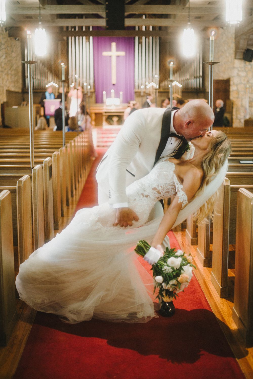 A romantic wedding photo series in a church with a couple posing playfully on red carpeted pews.