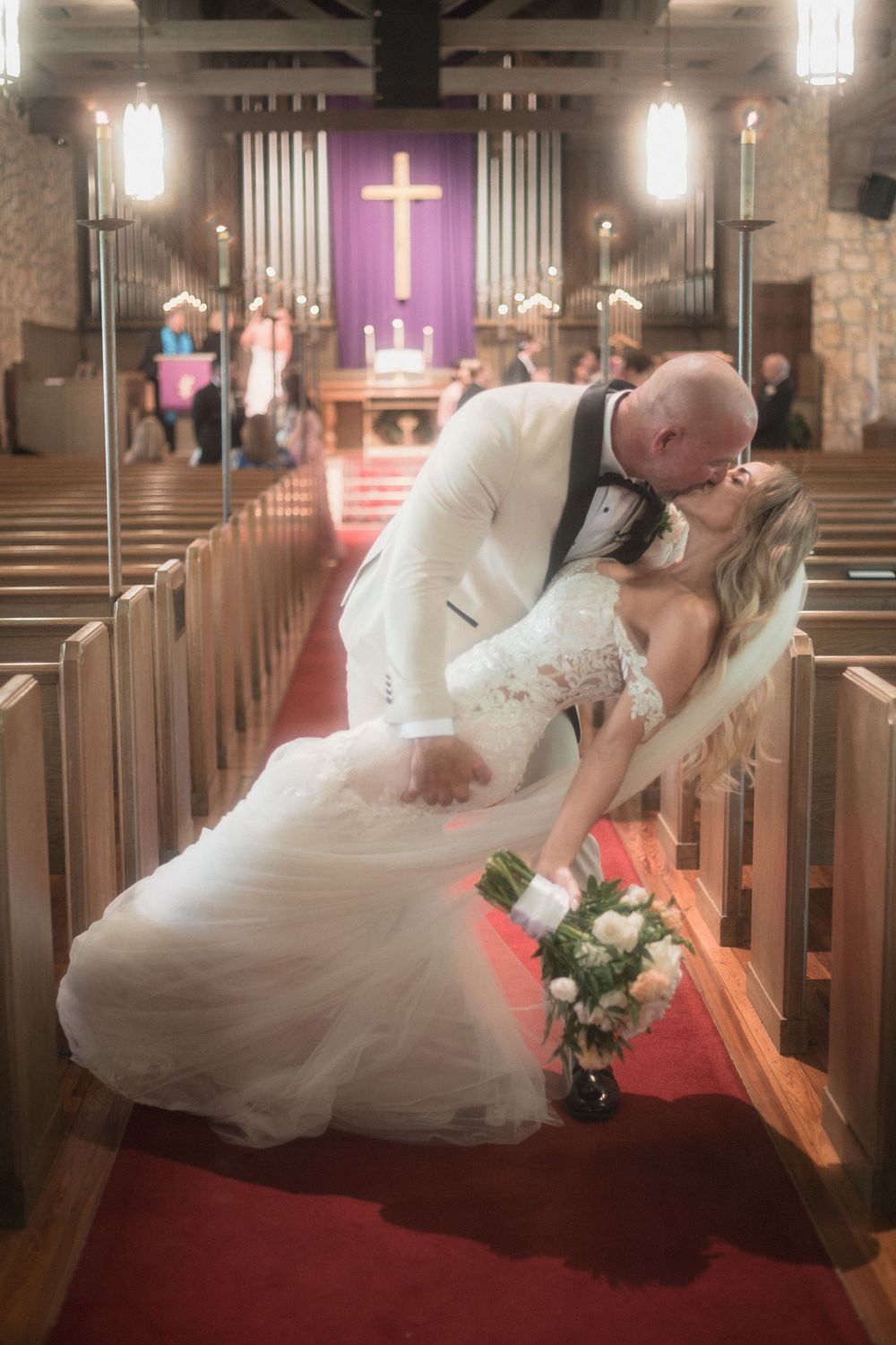 Bride and groom share a romantic dip kiss on the red carpet aisle of a church after their wedding ceremony.