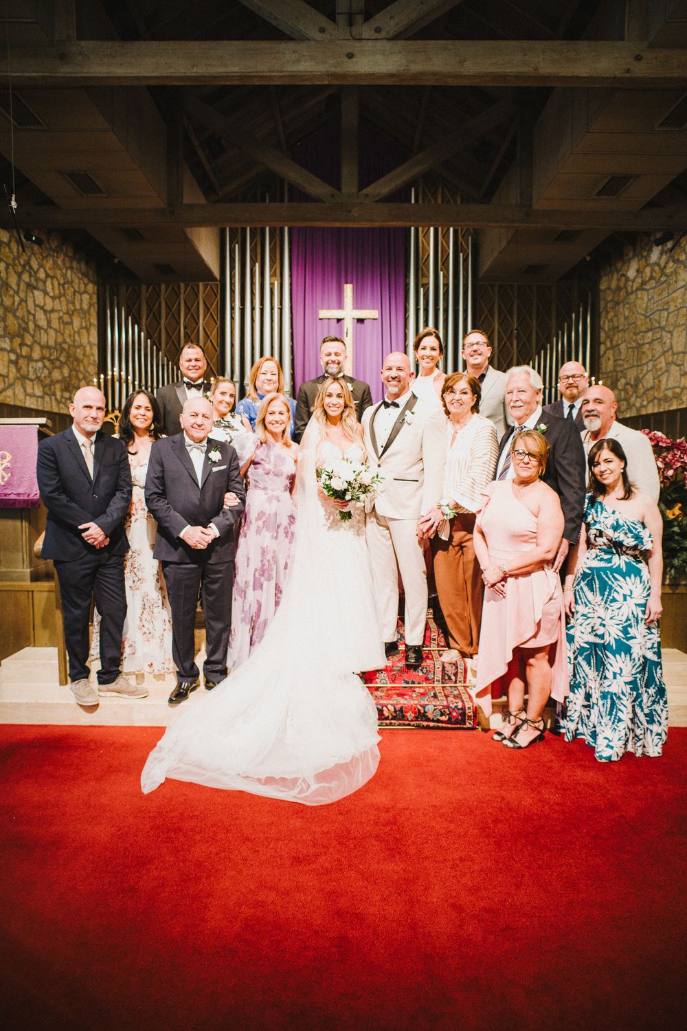Wedding party members pose together on red carpet in front of organ pipes during formal group photos.