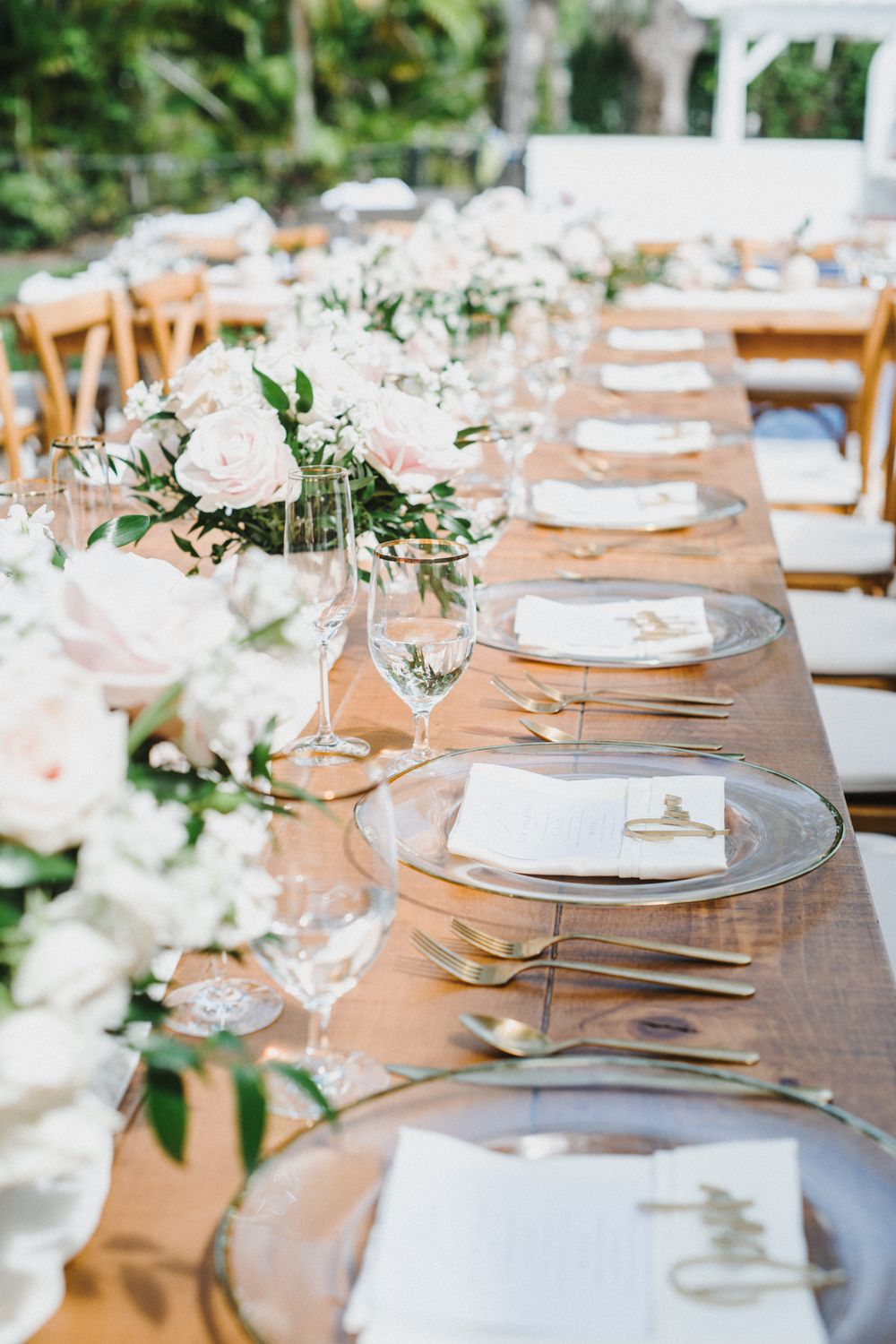 Elegant wedding reception table settings with white floral centerpieces, clear charger plates and wooden farmhouse tables.