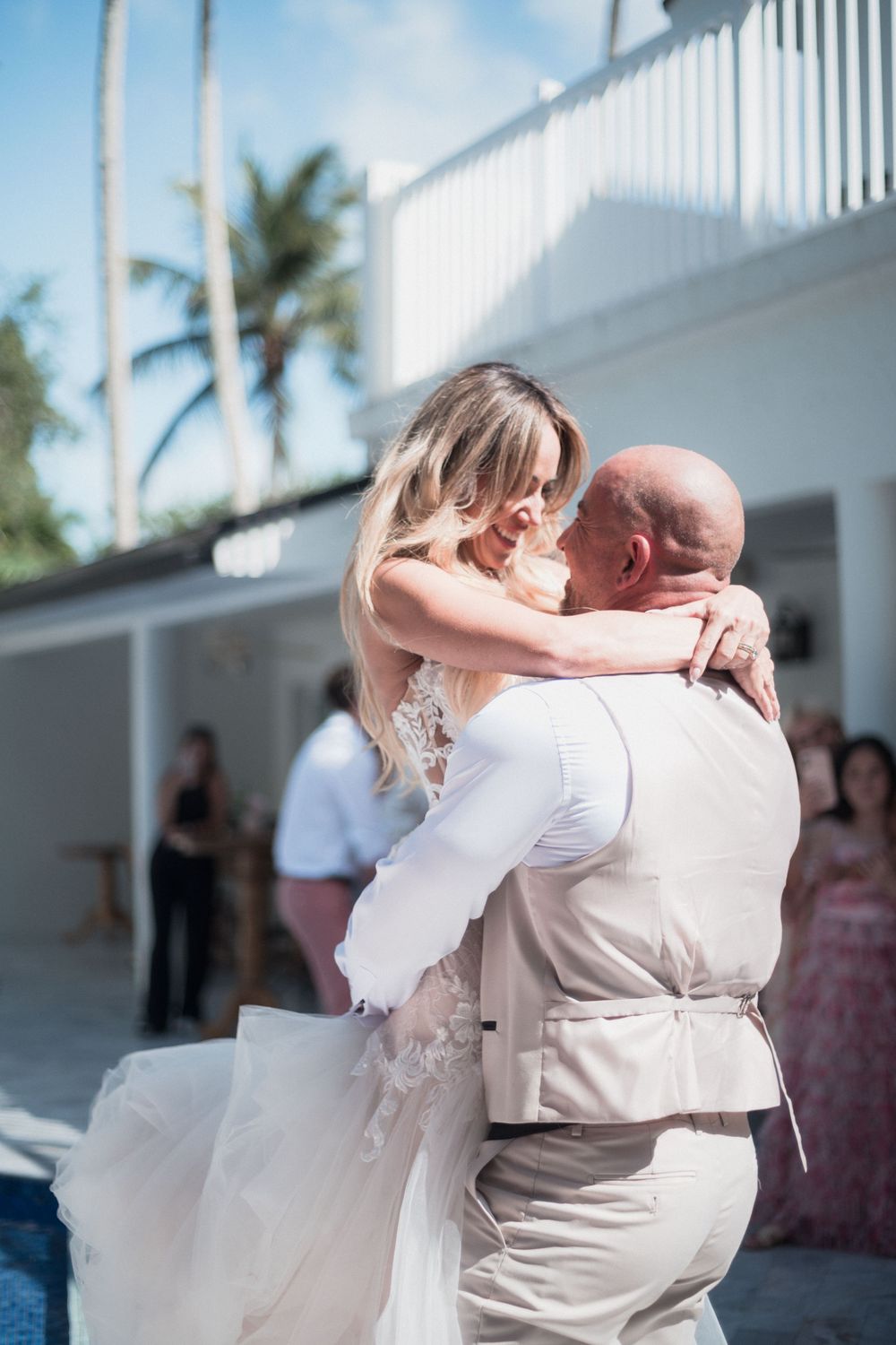Bride and groom share an emotional first dance embrace at outdoor tropical wedding venue with palm trees.