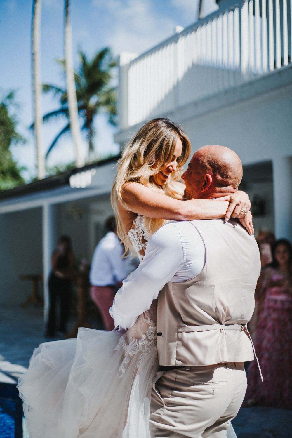 Emotional wedding dance moment captured on a bright patio with palm trees in the background.