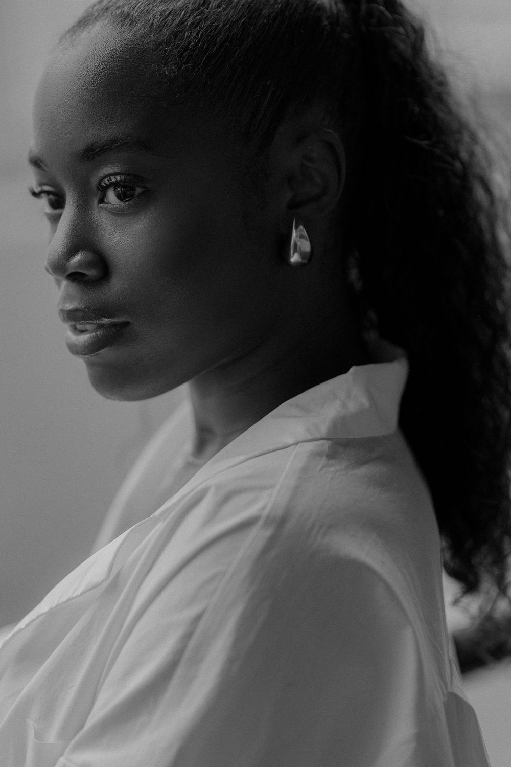 A black and white photo series showing profile views of a figure with curly hair wearing a white shirt against a dark background.