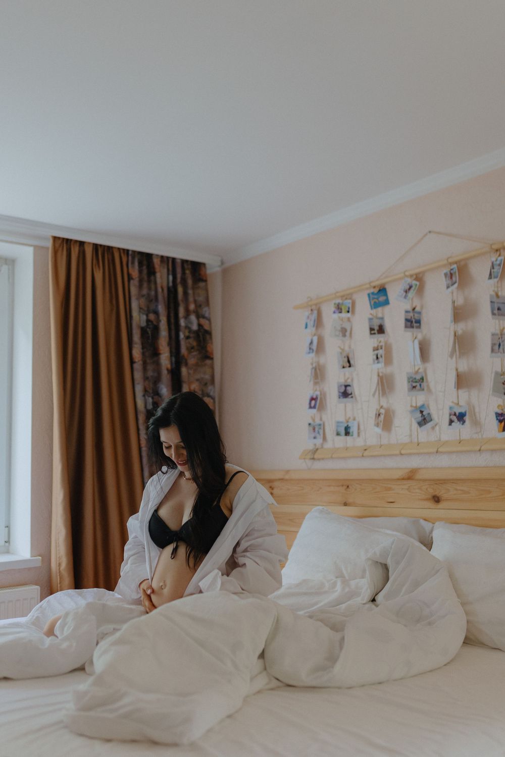 A person relaxes on a bed with white linens beneath a wall decorated with photographs in a cozy bedroom.