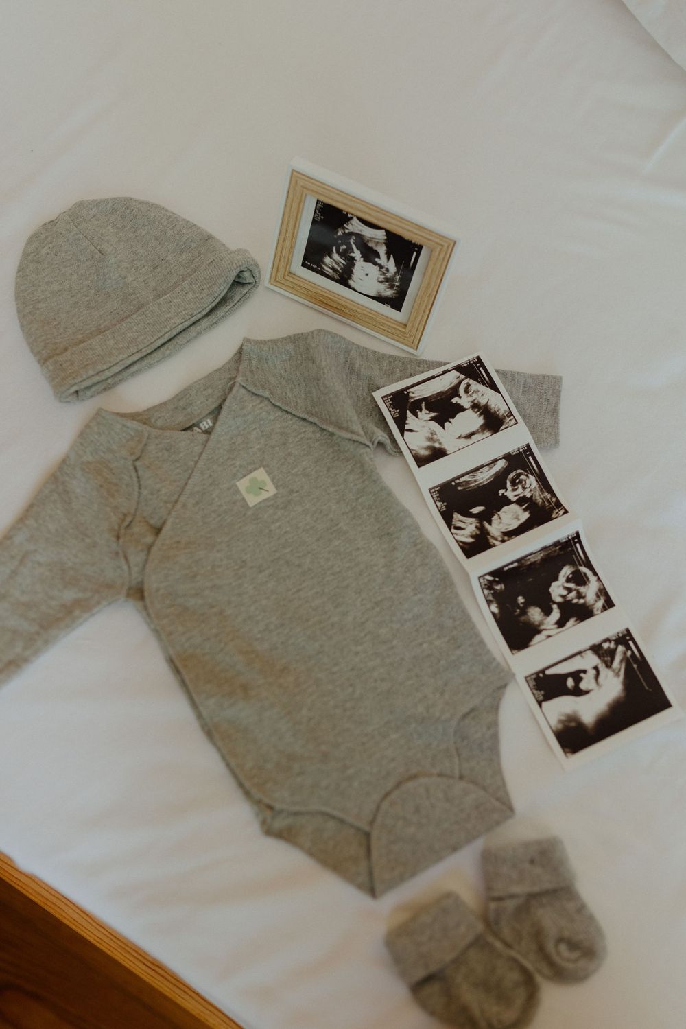 A gray hoodie sweatshirt laid flat on white bedding with vintage black and white photographs arranged beside it.