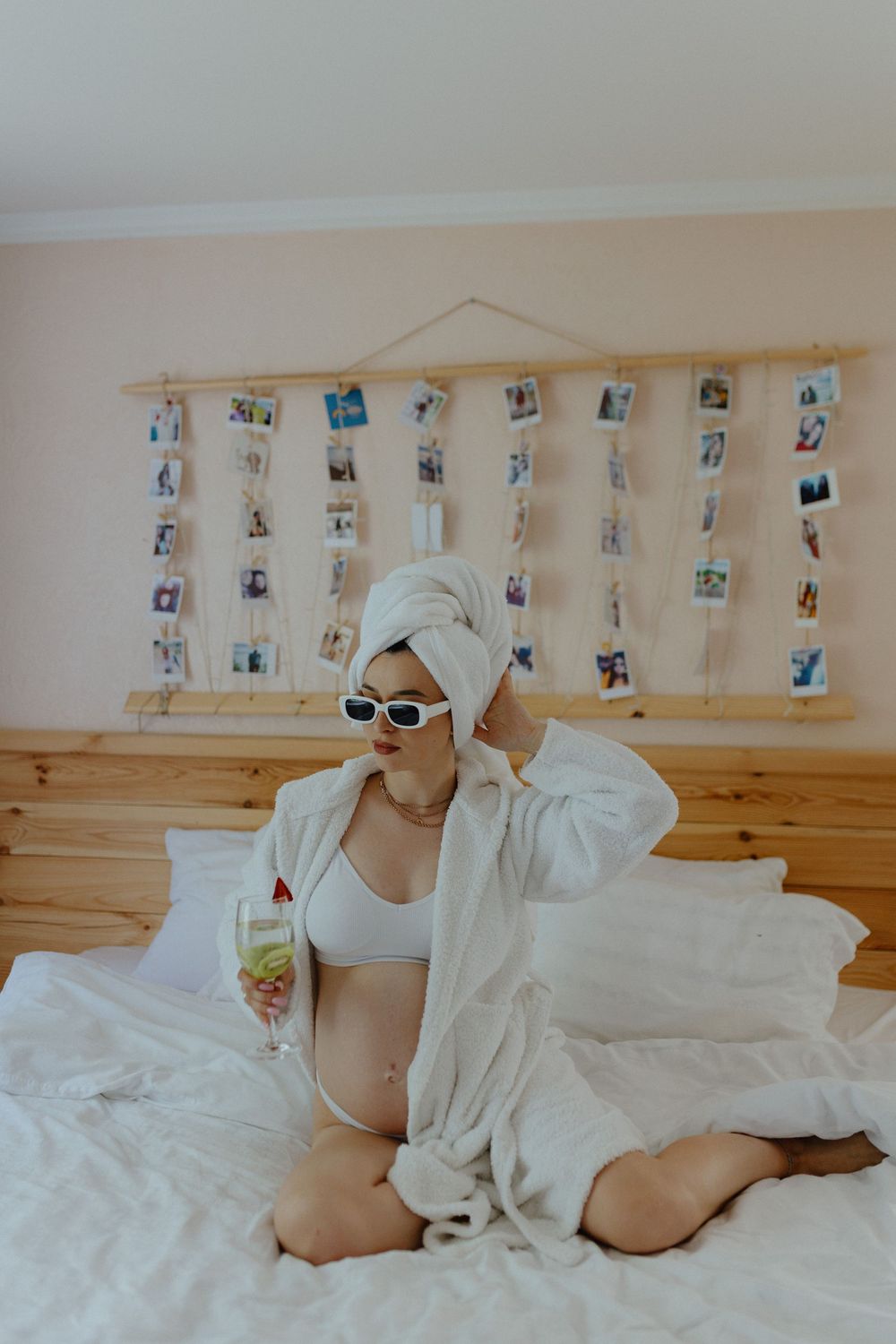 Woman in white robe and bra relaxing on bed with photo display wall in background.