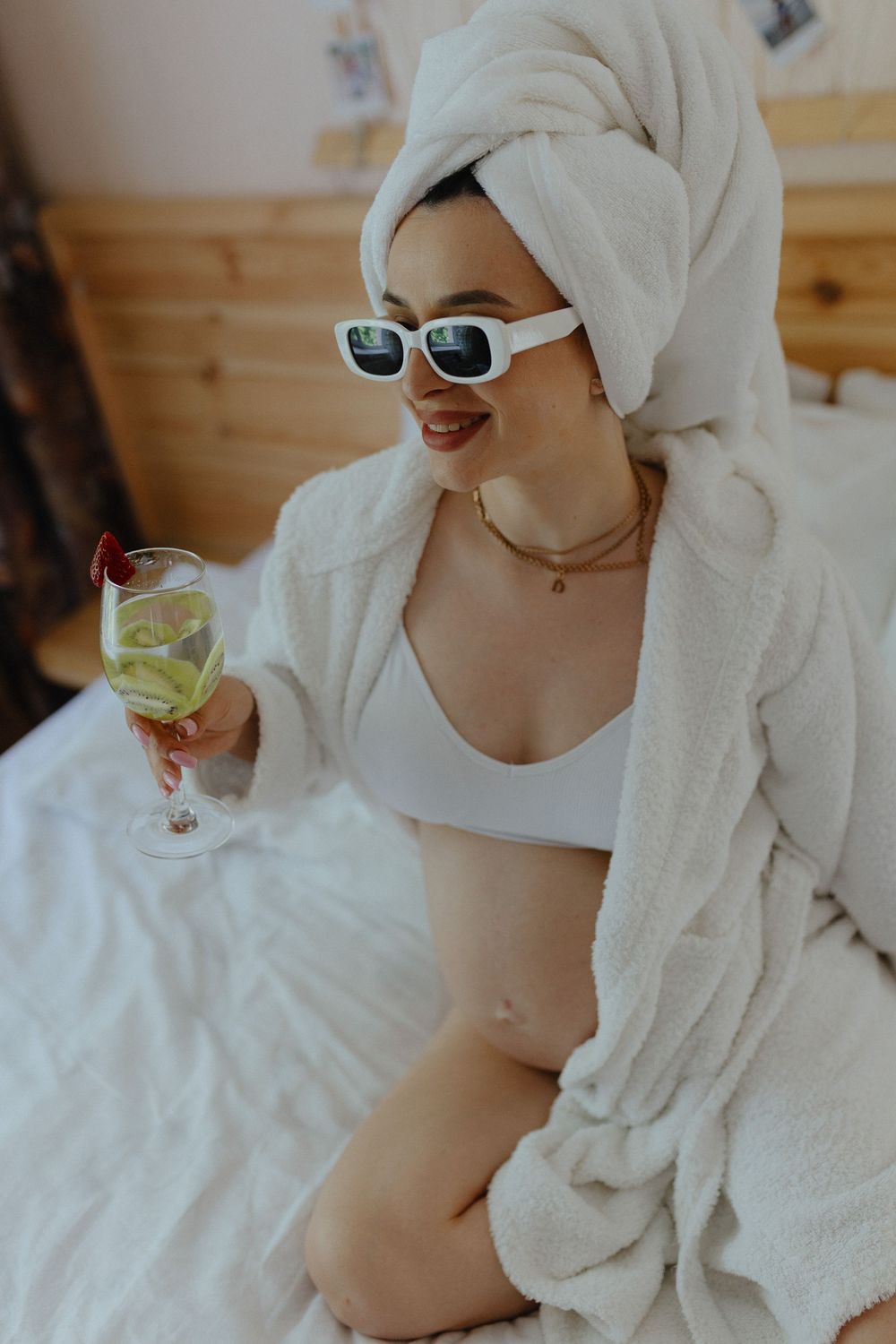 Person relaxing in white bathrobe and towel wrap enjoying a refreshing drink with lime on a sunny morning.