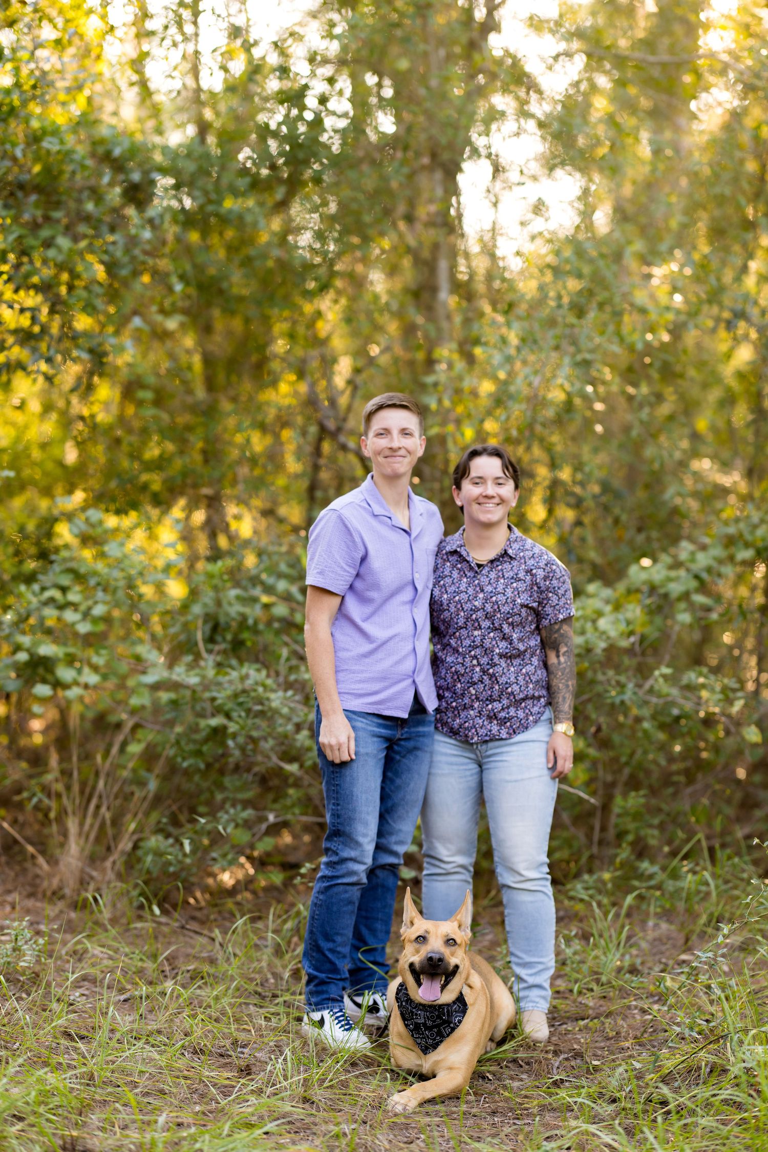 A family poses together in a natural outdoor setting with golden sunlight filtering through autumn trees.
