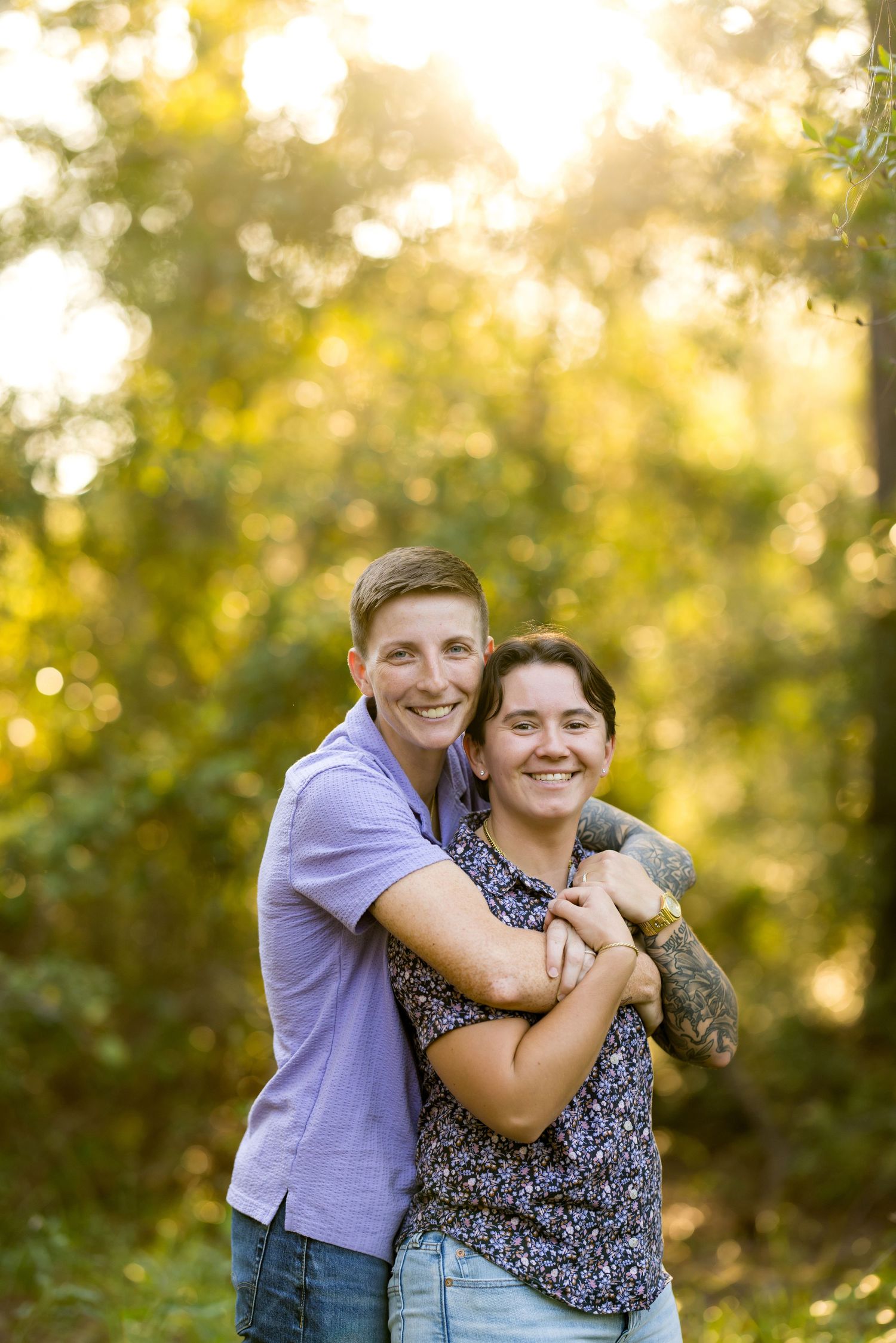 Happy couple embraces while holding their cat outdoors in warm golden sunlight with bokeh background.