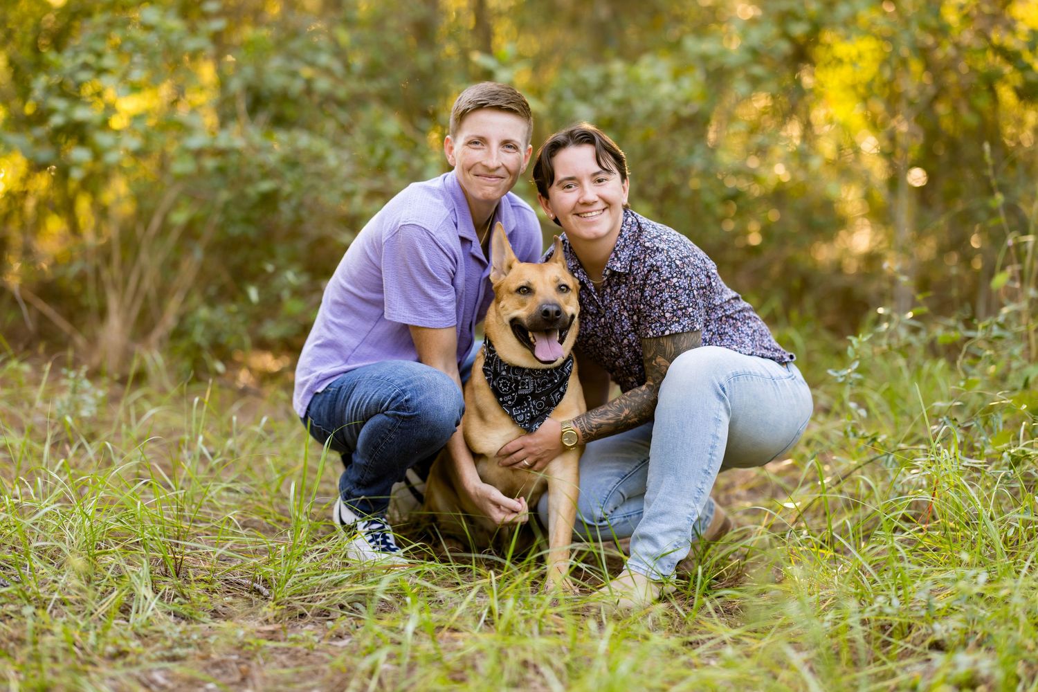 A couple poses with their German Shepherd dog in a grassy outdoor setting during autumn.