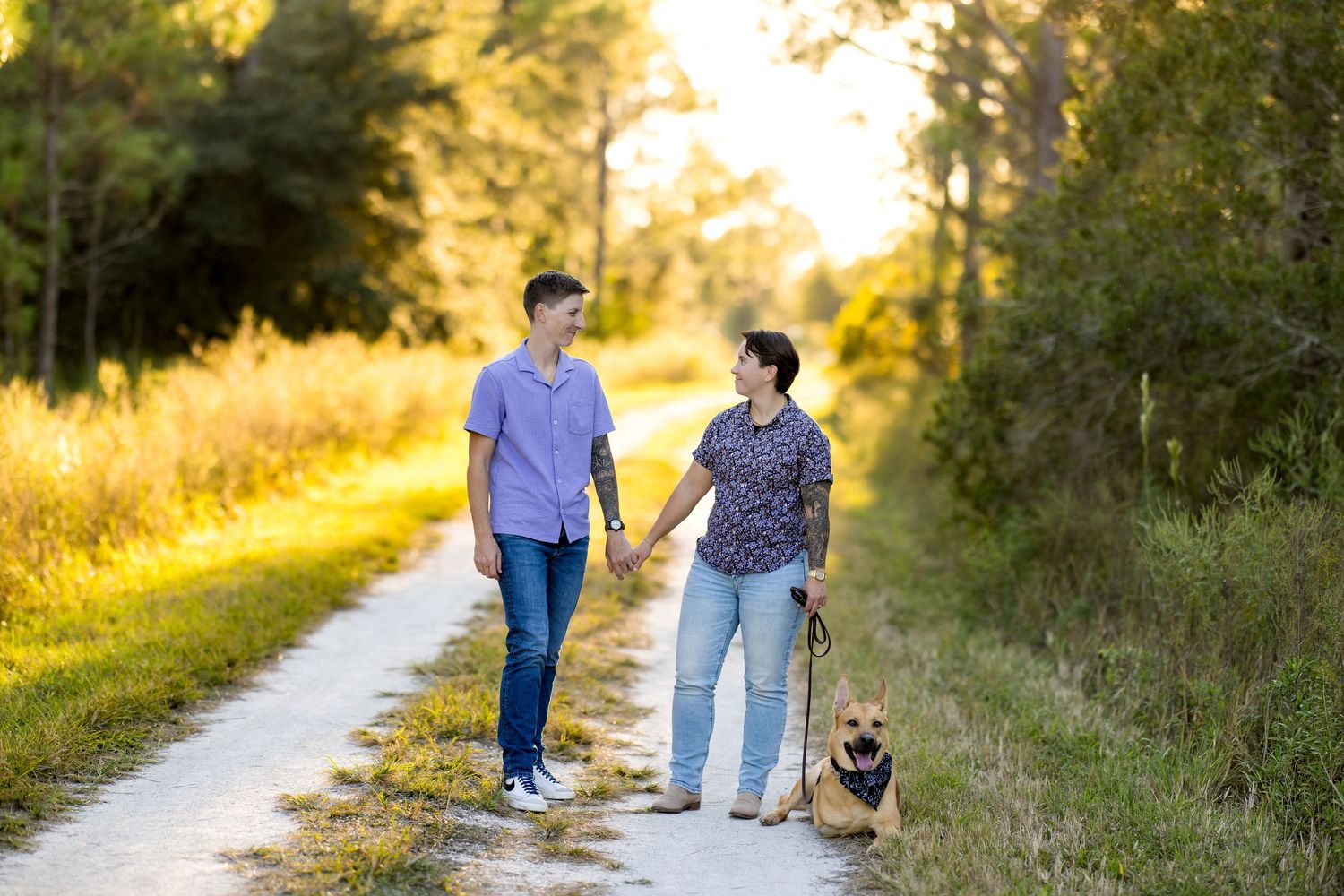 A couple walks together on a sunlit path through nature during golden hour while holding hands.