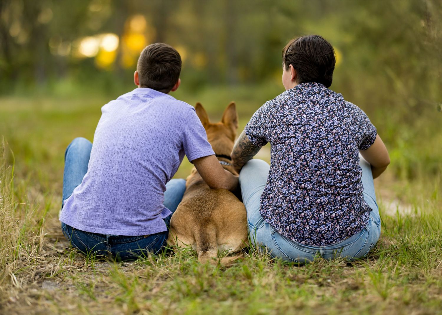 Two people sit together on grassy ground in a relaxed outdoor setting.