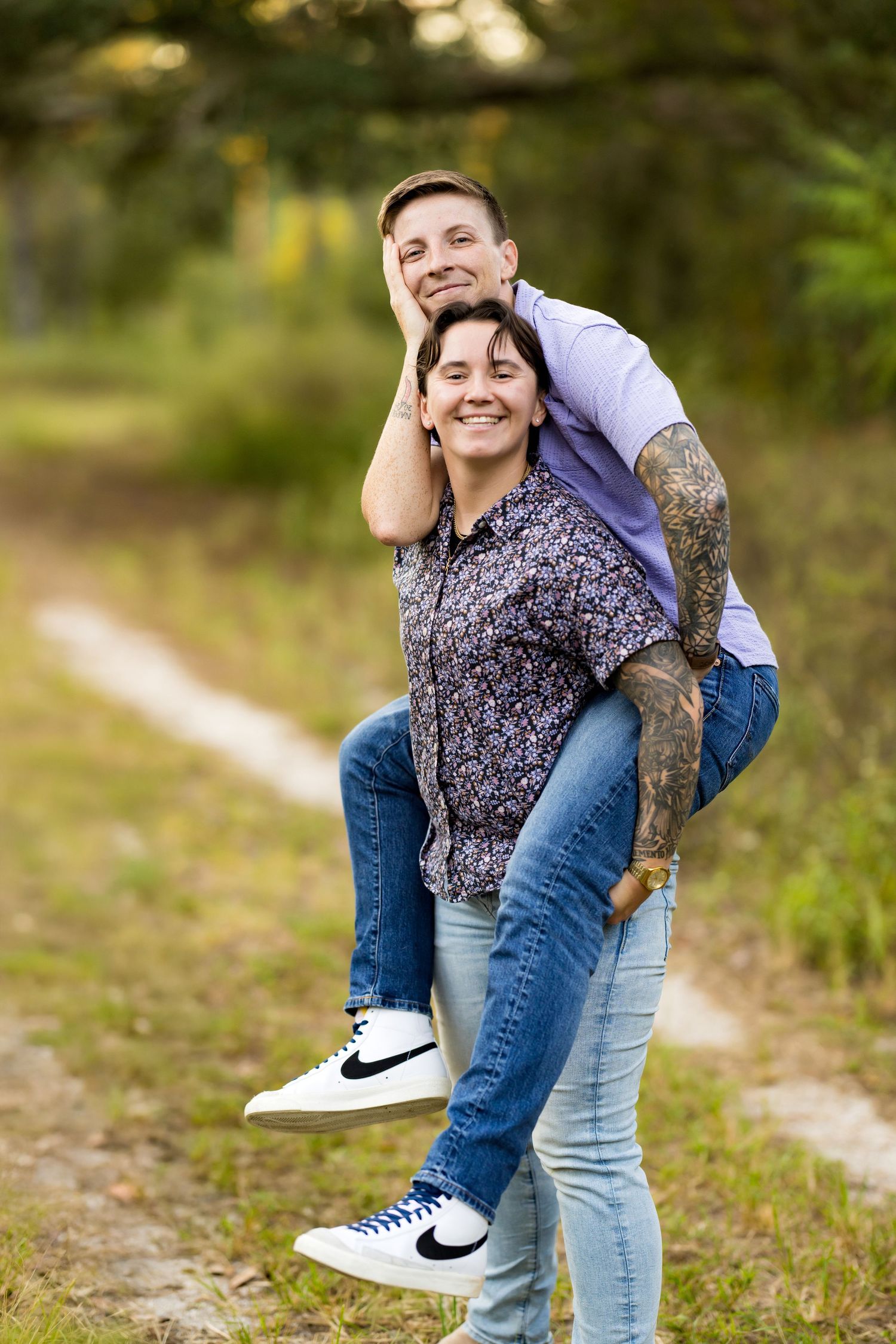 A couple shares a playful moment outdoors while sitting on a wooden fence in a natural setting.
