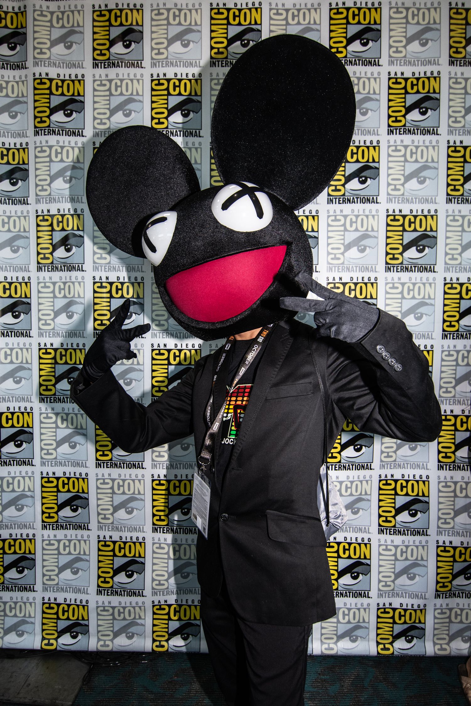 A person in a black and red deadmau5 costume stands playfully, showcasing large ears and a cheerful expression.