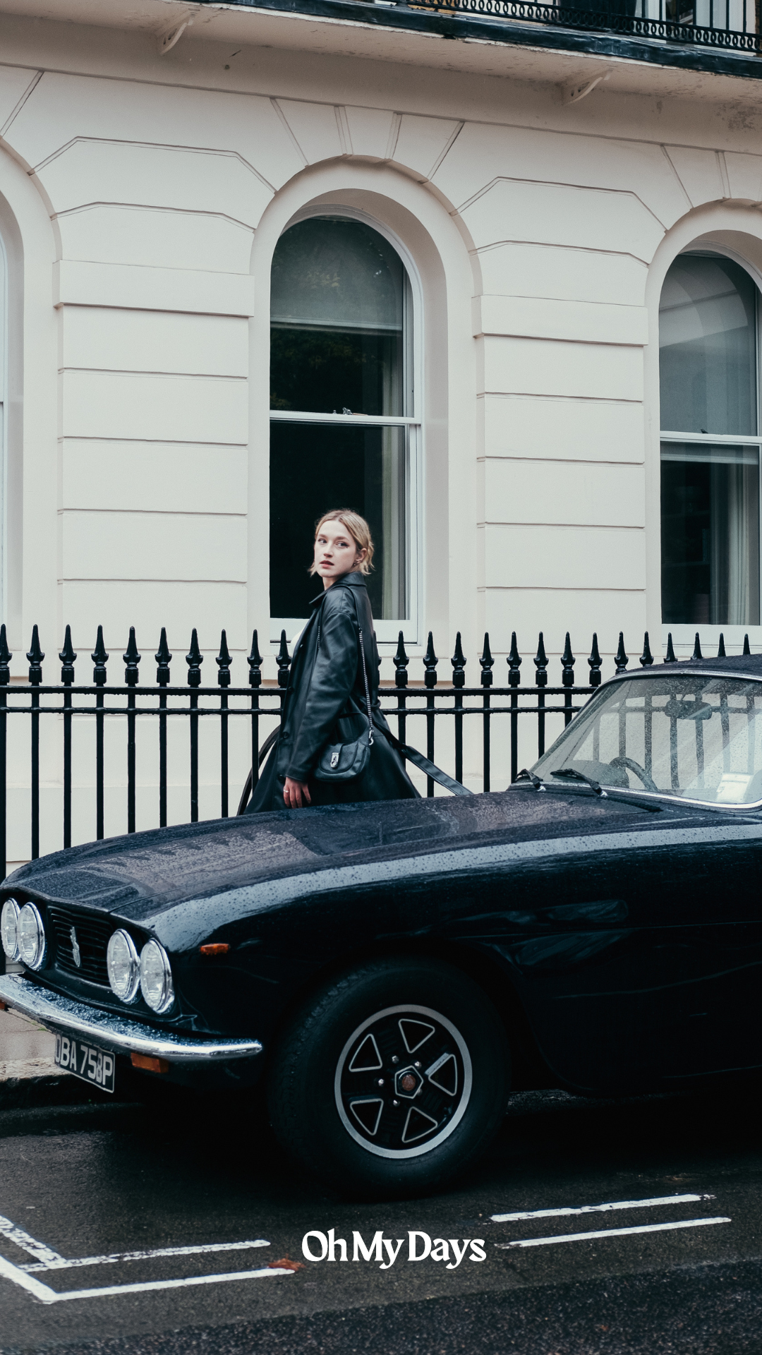Classic black convertible car parked in front of elegant white townhouse with wrought iron fence in London.