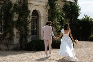 Newlyweds walk hand in hand towards an ivy-covered building entrance.