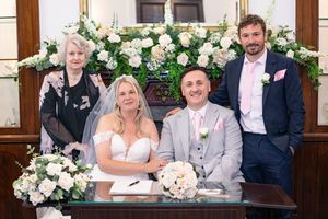 Wedding party gathered around floral arch with white and cream flower arrangements.