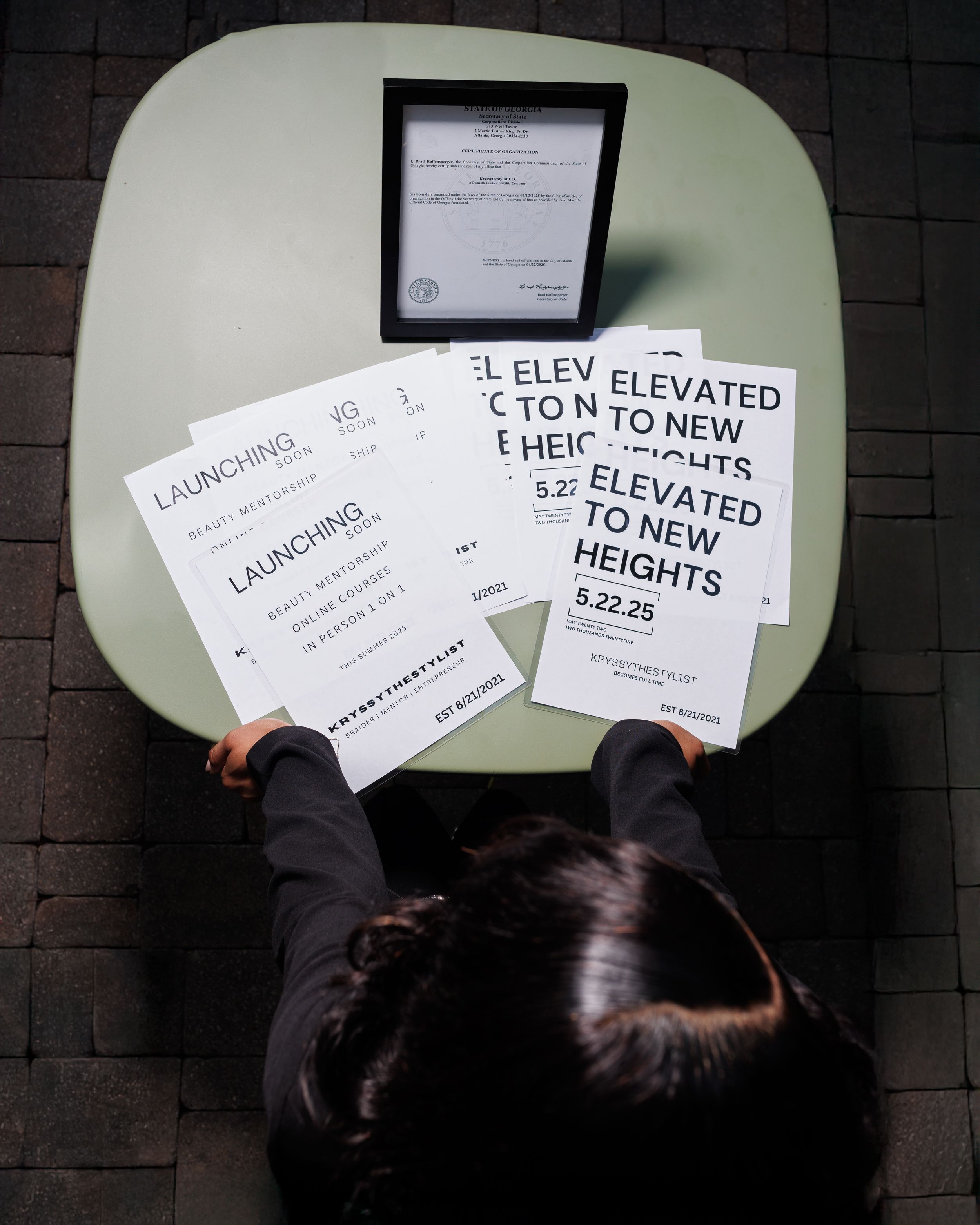 Multiple paper signs with text including 'ELEVATED' and 'HEIGHTS' are held up against a light green wall background.