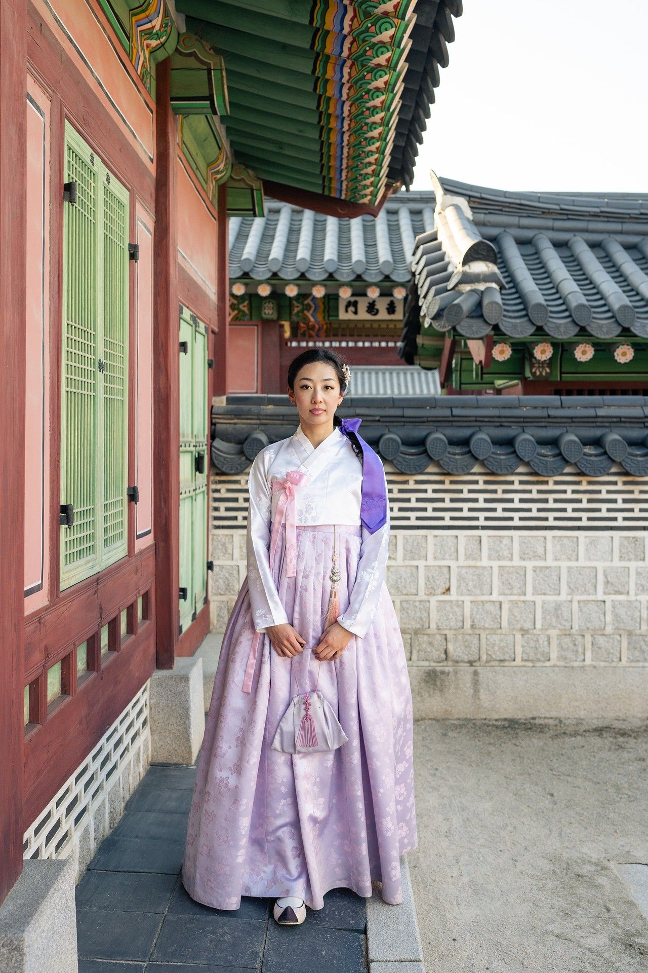 Traditional Korean hanbok dress worn in a historic palace courtyard with traditional architecture visible in background.