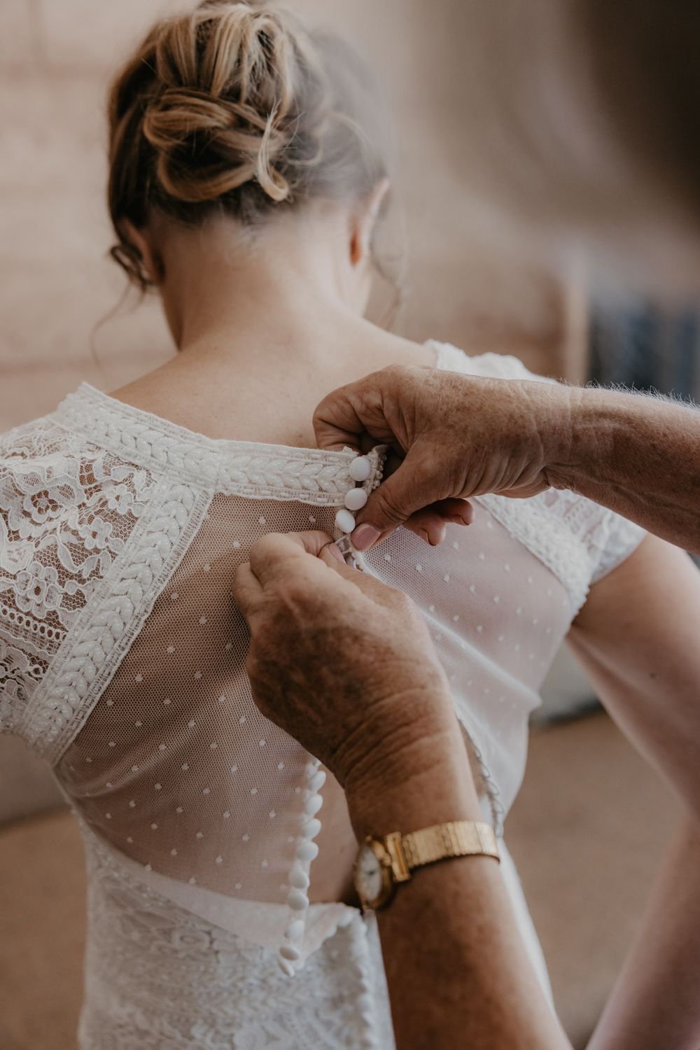 Close up of brides back with hands of mother doing up all the buttons on wedding dress