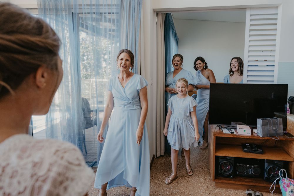 Smiling happy bridesmaids seeing bride in dress for the first time during reveal
