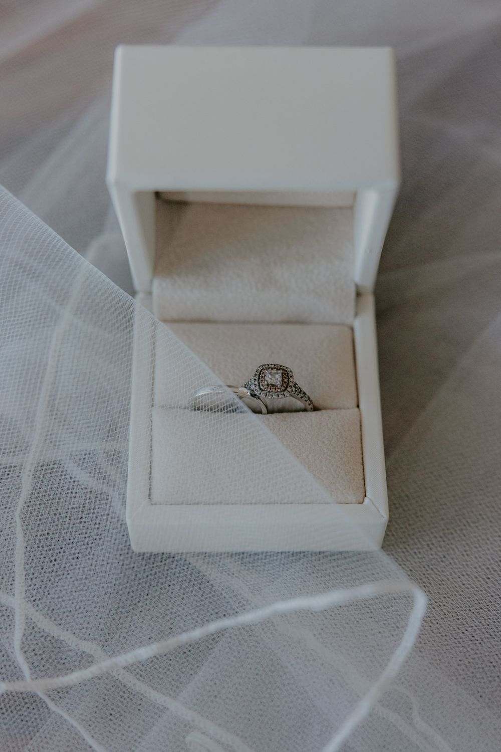 Ring box open with engagement ring and wedding band next to each other with part of veil wrapped over the rings