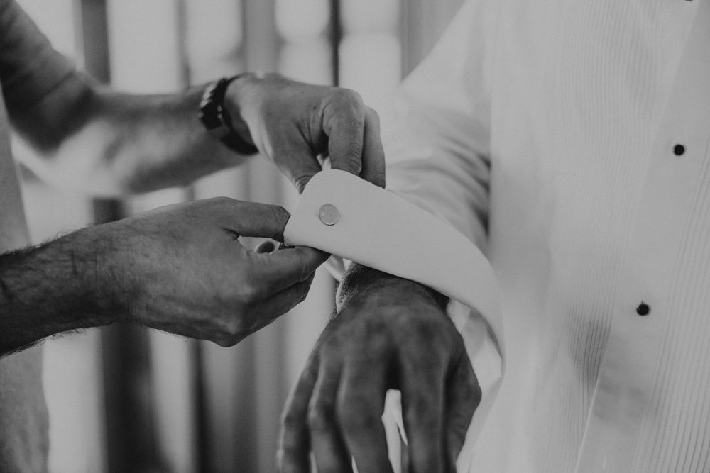 Best man helps insert cufflinks into grooms white dress shirt prior to wedding