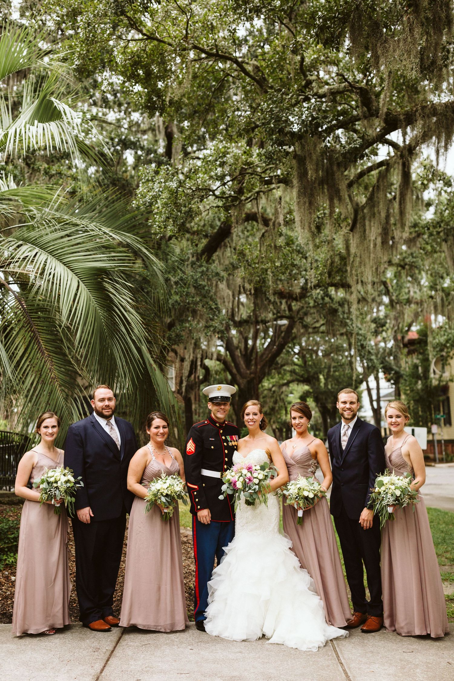 Wedding party poses outdoors under Spanish moss draped trees with bridesmaids in dusty rose dresses.