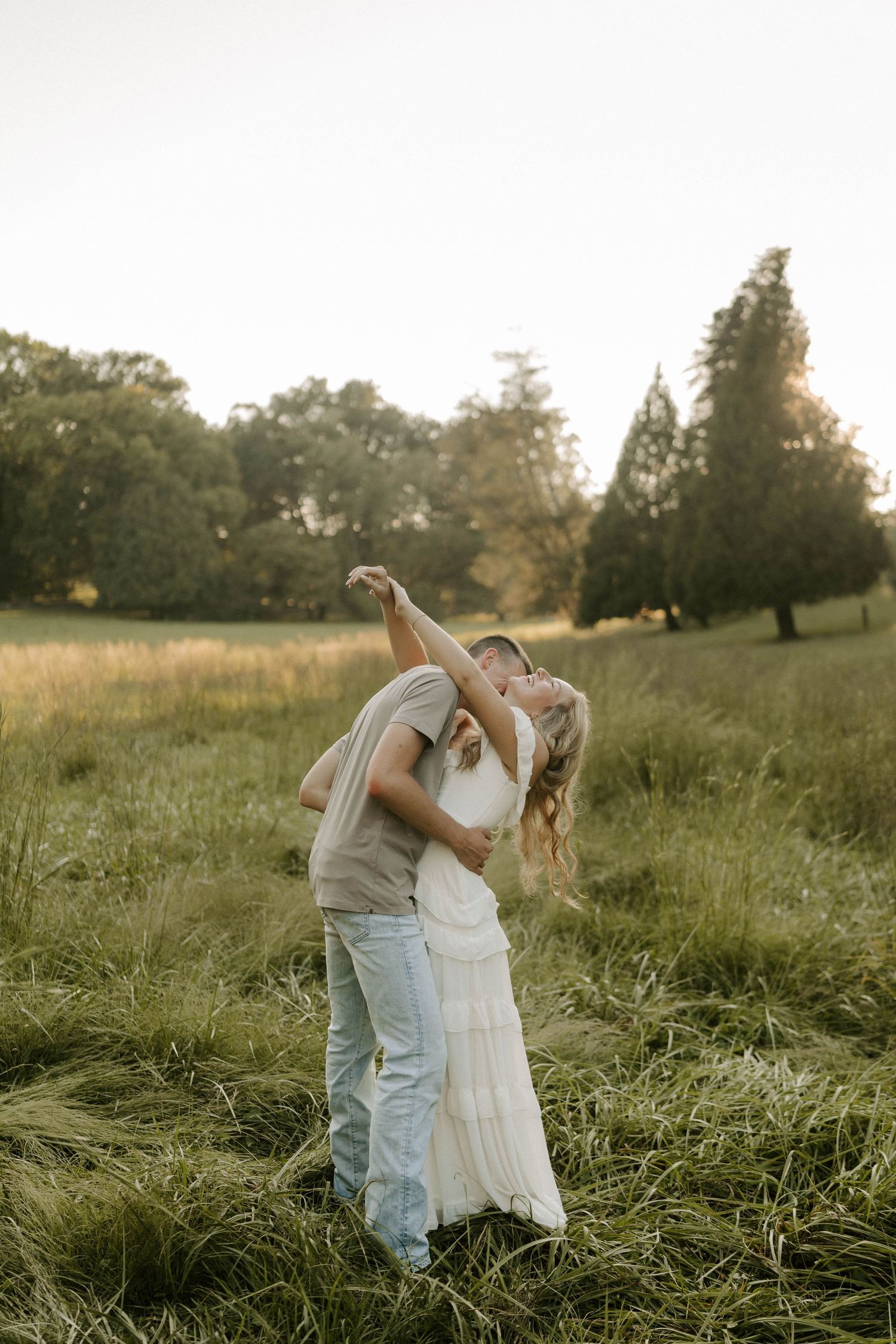 Couple sharing romantic moment on stone path surrounded by lush green trees in sunlit garden.