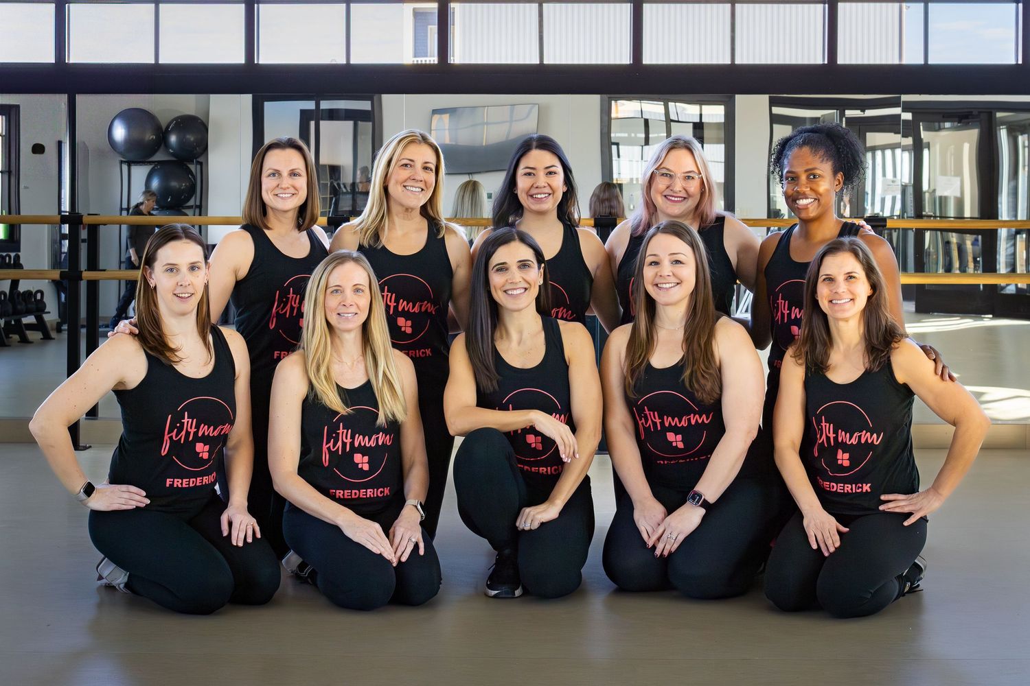 Fitness instructors in matching black tank tops pose together on studio floor during group photo session.