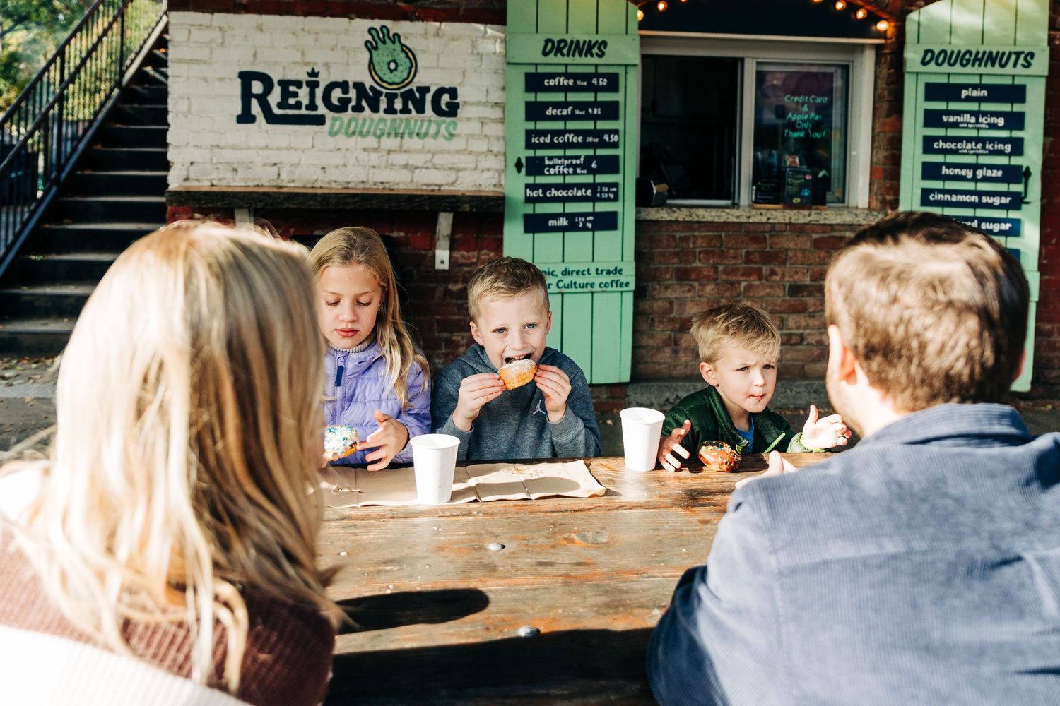 People gather at an outdoor restaurant patio with wooden tables and rustic decor visible in the background.