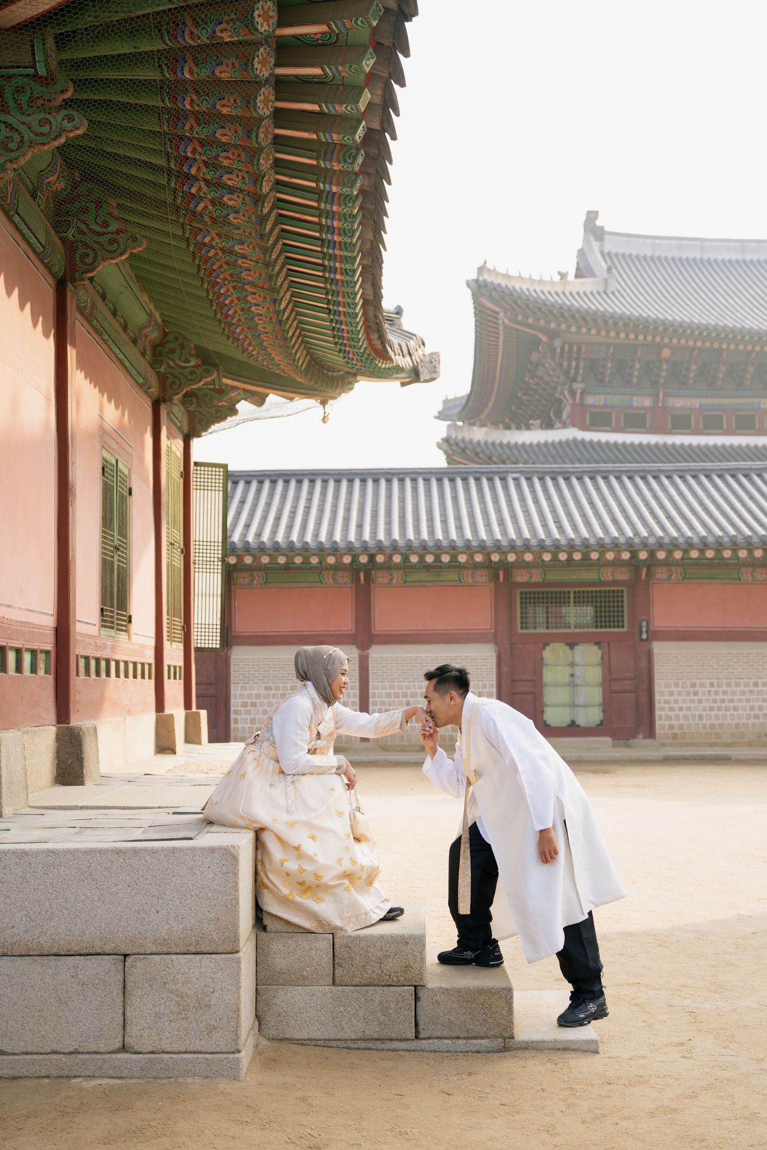 Traditional Korean hanbok-clad figures bow gracefully to each other in a historic palace courtyard.